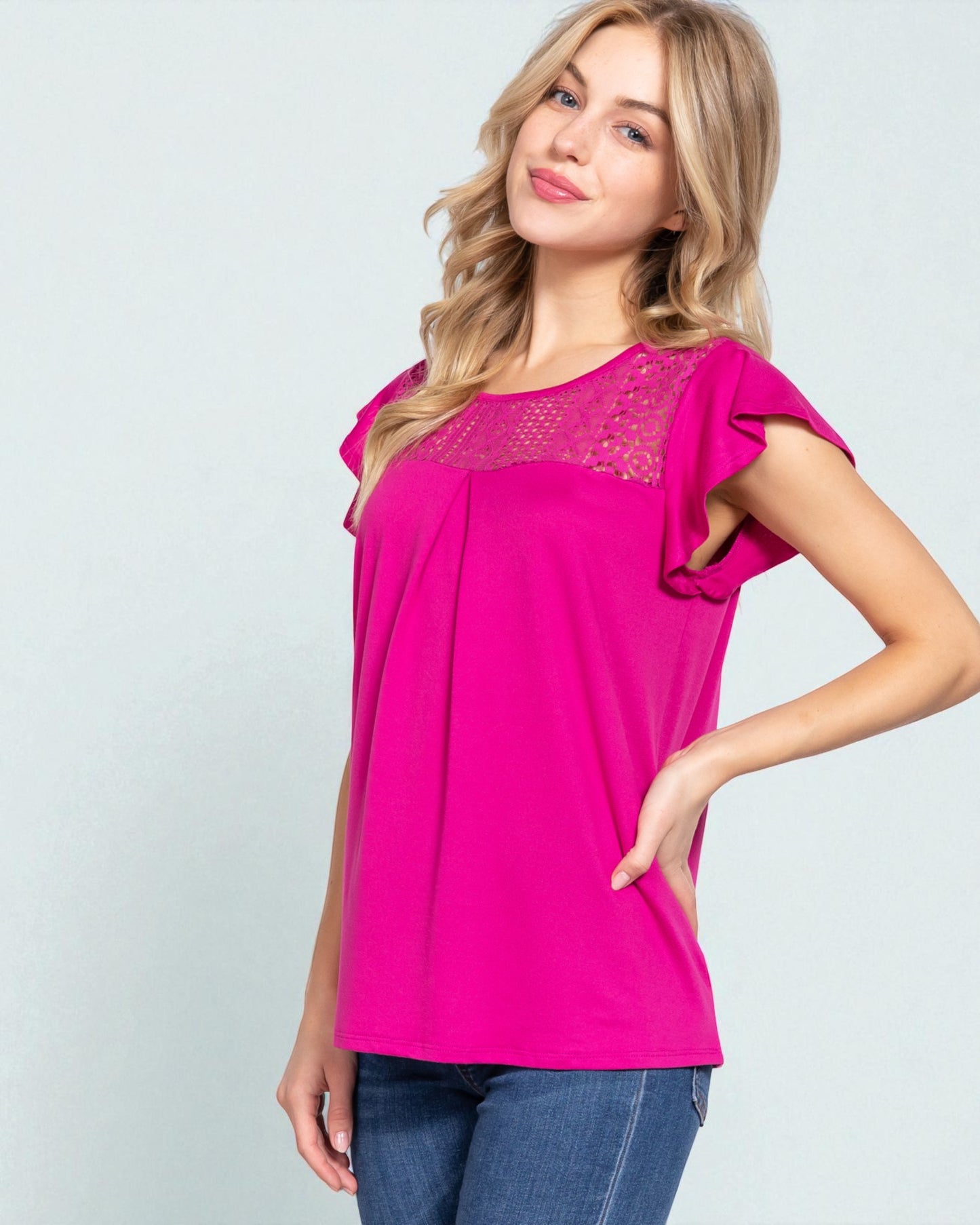 Woman wearing a bright pink top with lace details on a light gray background