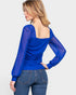 Woman wearing a blue long-sleeve top with sheer sleeves on a white background