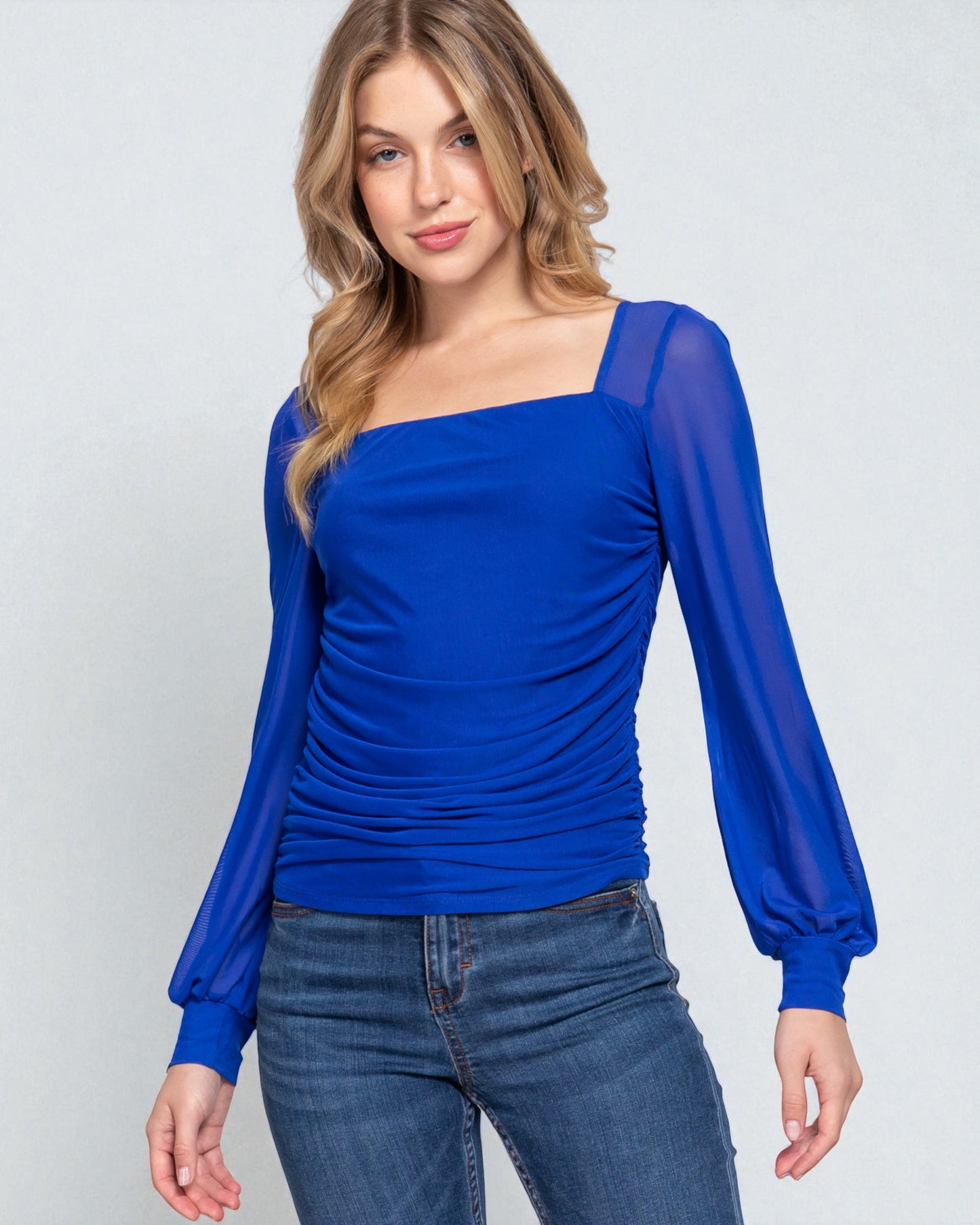 Woman wearing a blue top with sheer sleeves on a light gray background