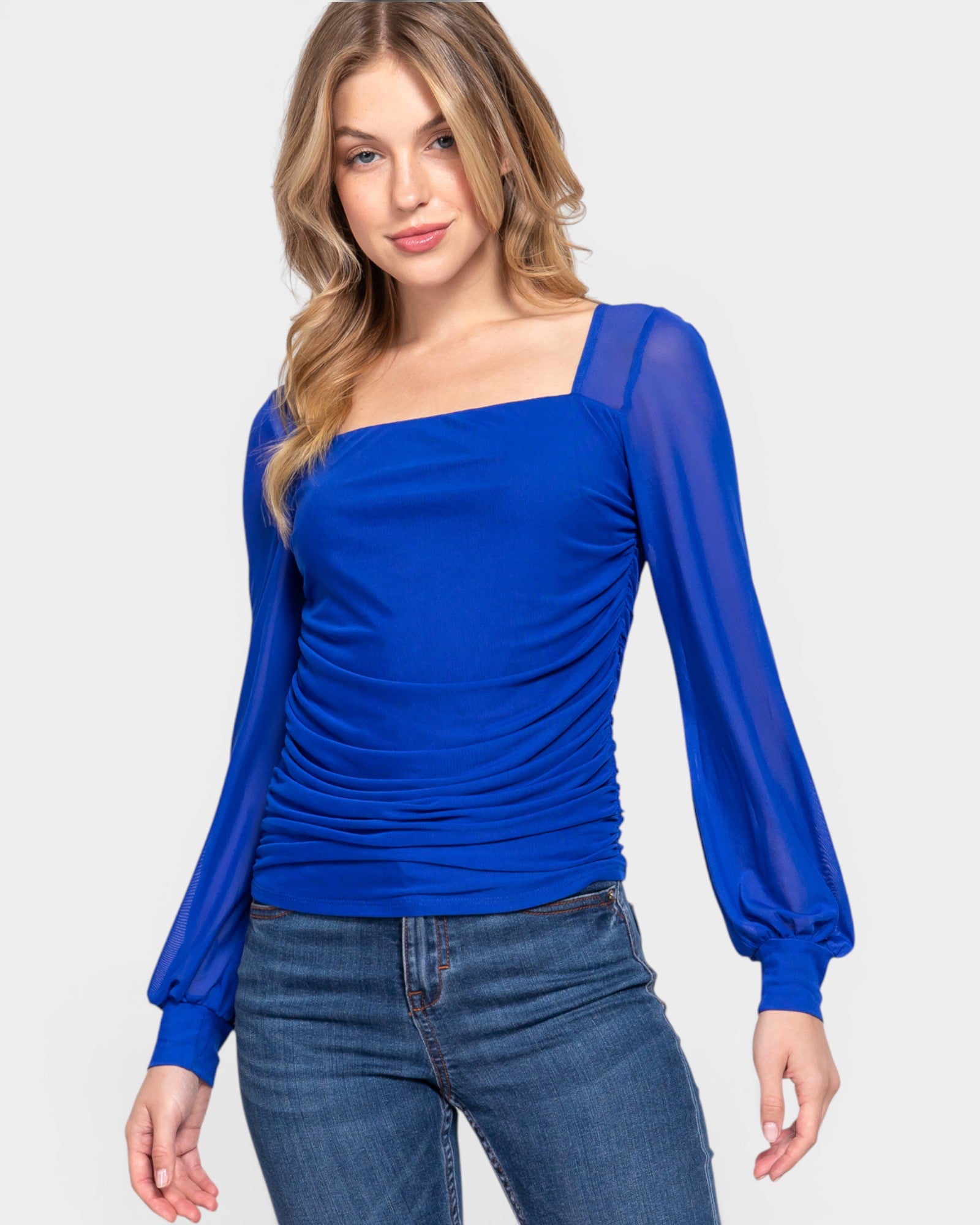 Woman wearing a blue top with sheer sleeves on a light gray background