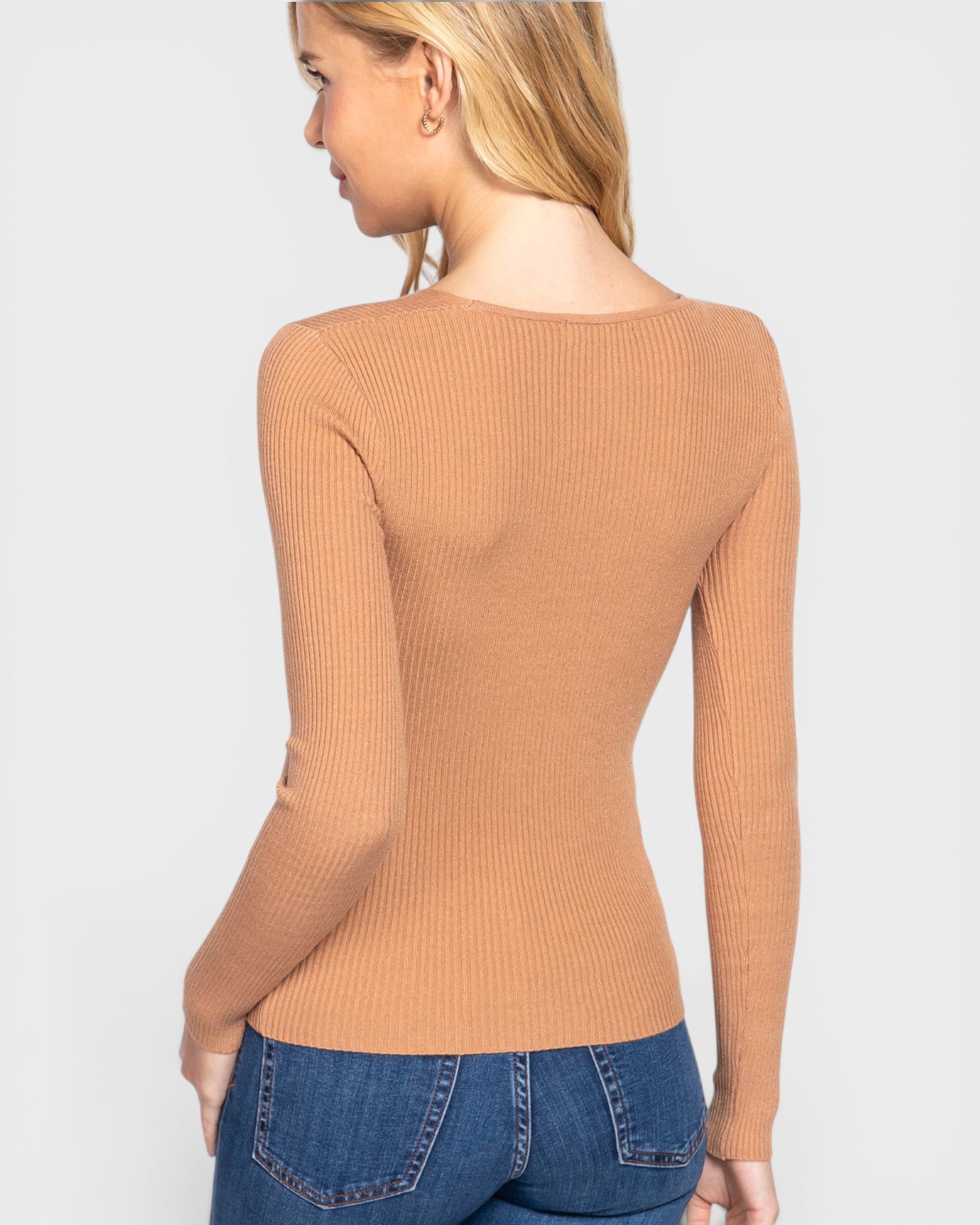 Woman wearing a brown ribbed long-sleeve top and blue jeans on a white background