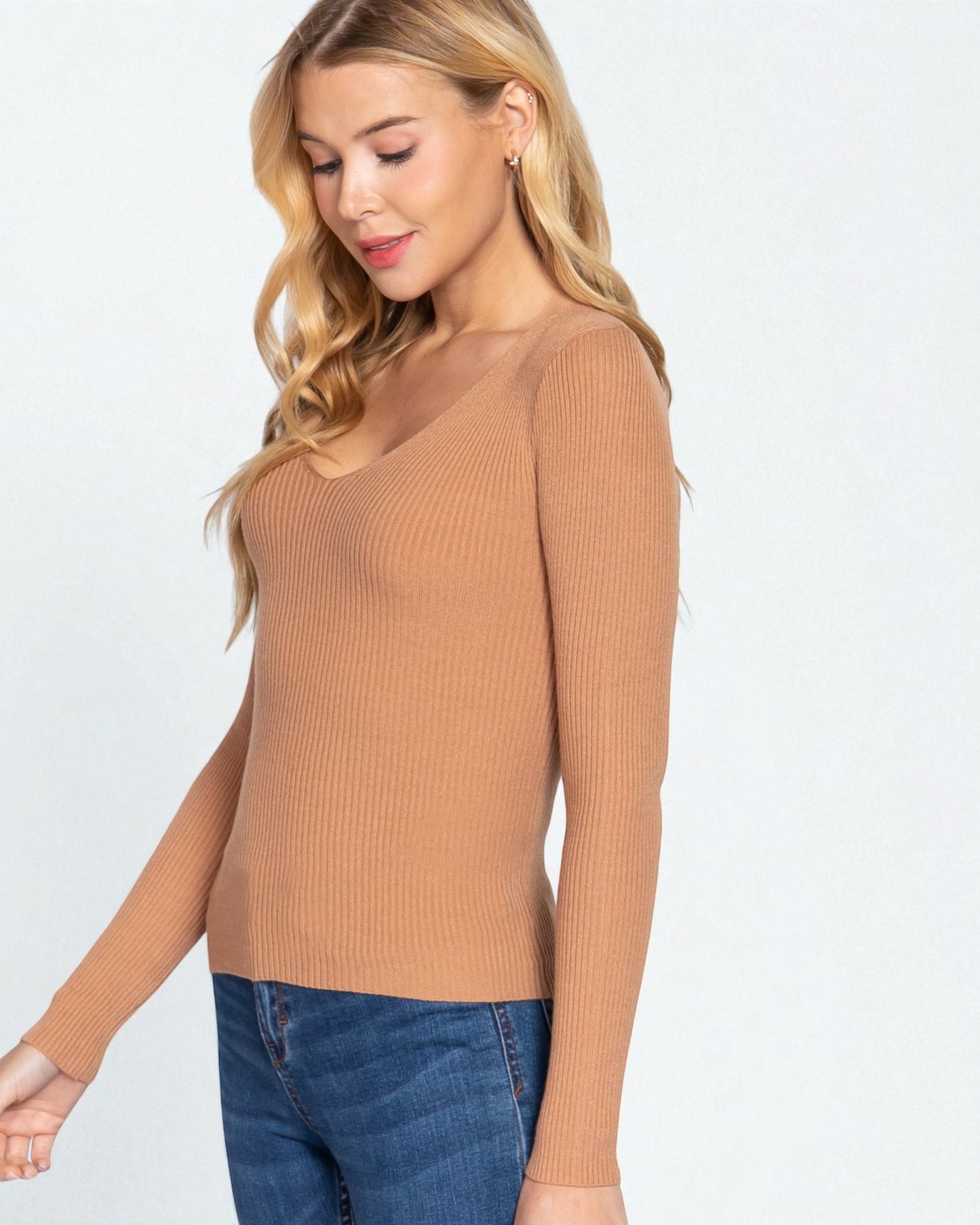 Woman wearing a brown ribbed sweater and blue jeans on a white background