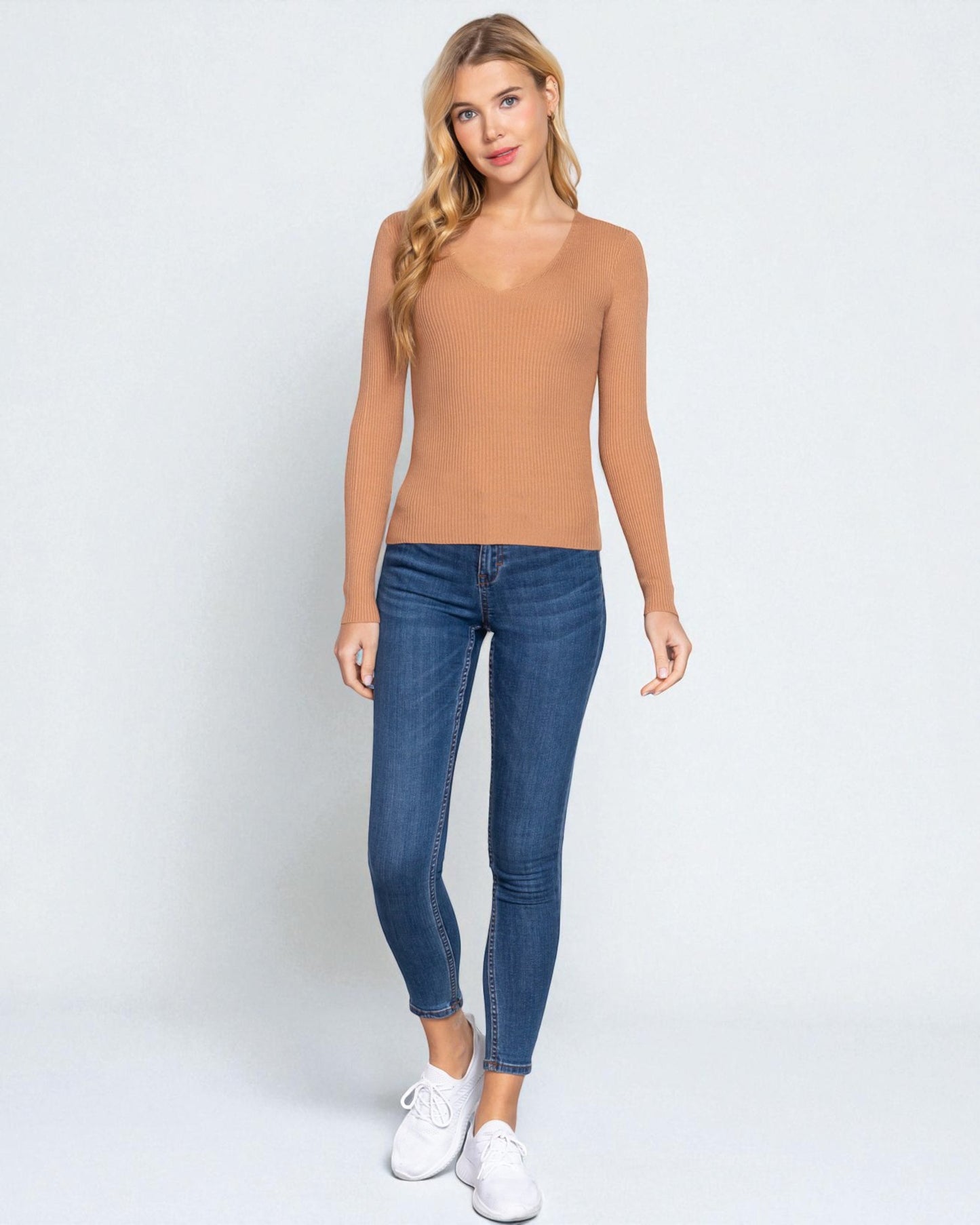 Woman wearing a tan top and blue jeans on a white background