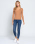 Woman wearing a tan top and blue jeans on a white background