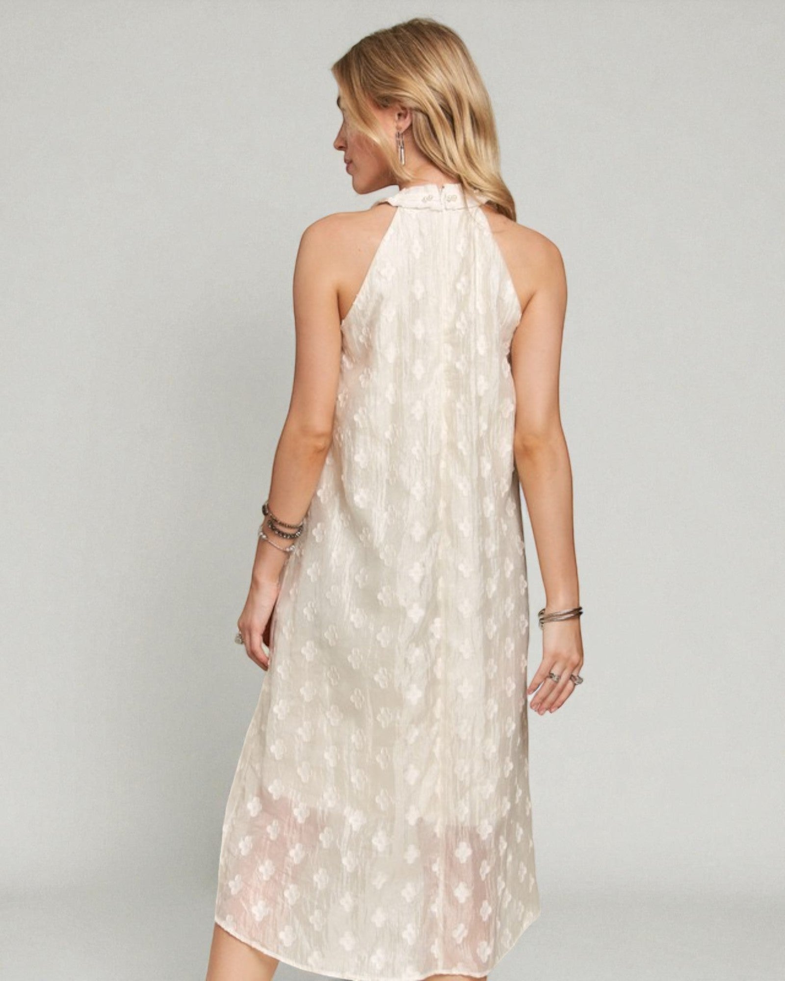 Woman wearing a white halter neck dress with floral patterns on a plain background