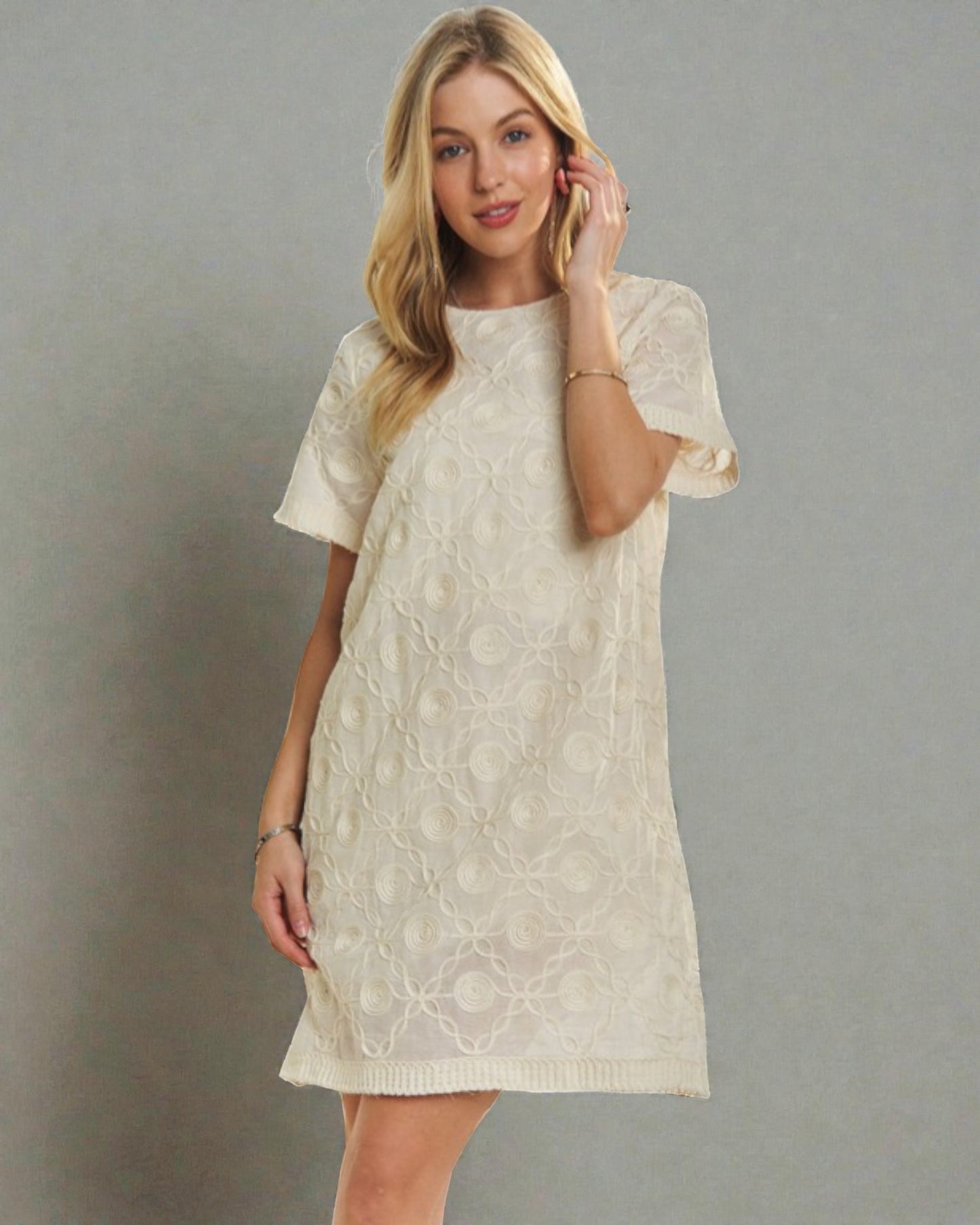 Woman wearing a beige lace dress against a gray background