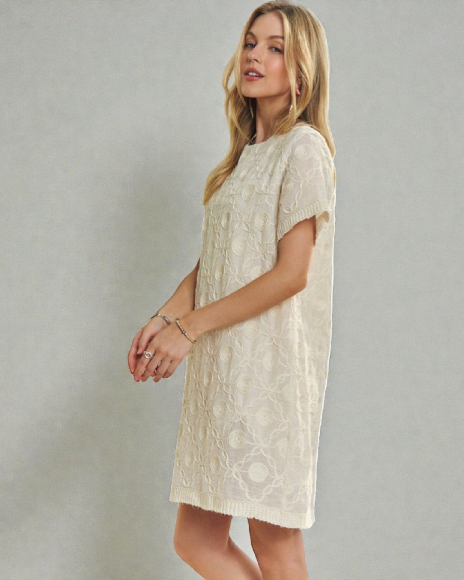 Woman wearing a beige lace dress against a plain background