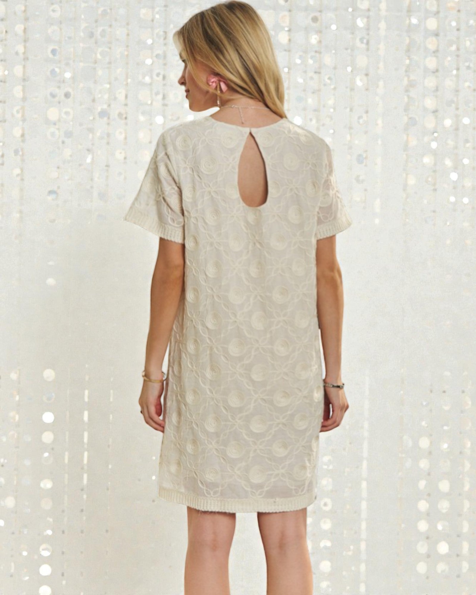 Woman wearing a beige lace dress with cut-out back against a white background