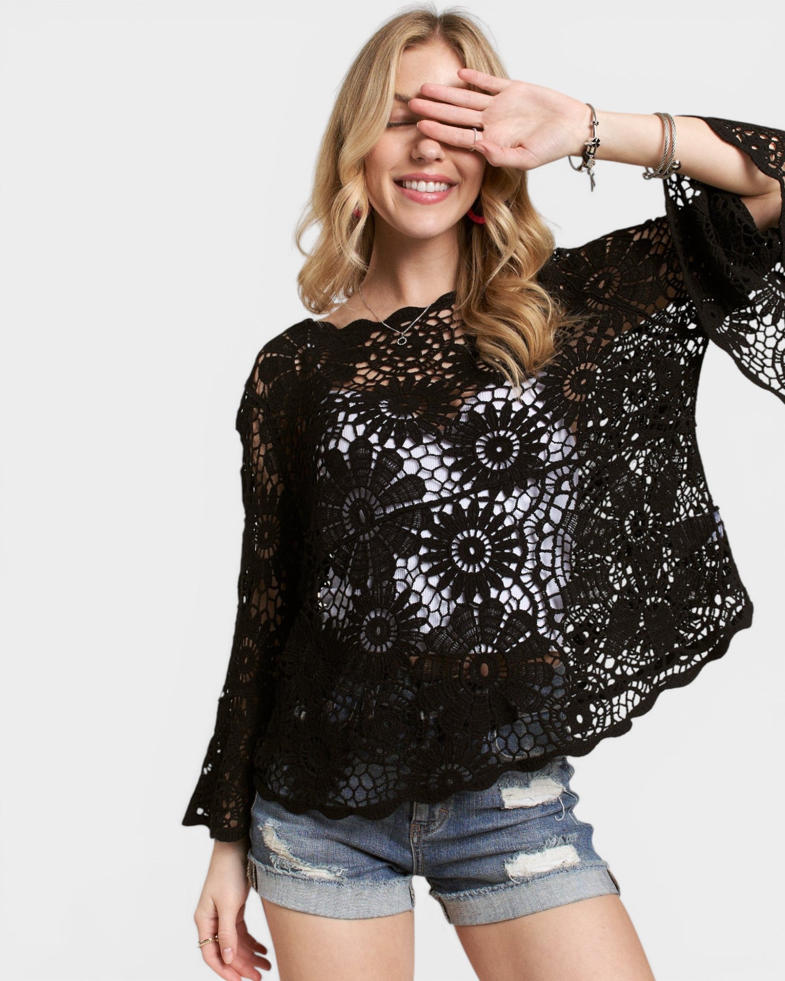 Woman wearing a black lace top and denim shorts on a plain background