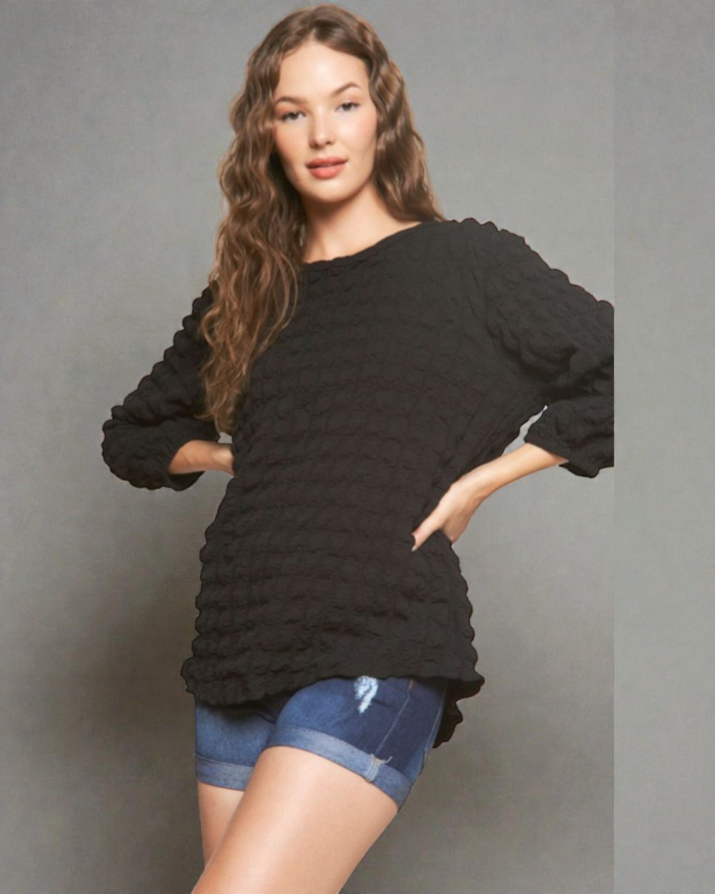 Woman wearing a black textured sweater and denim shorts against a gray background