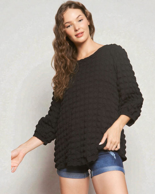 Woman wearing a black textured sweater and denim shorts on a plain background