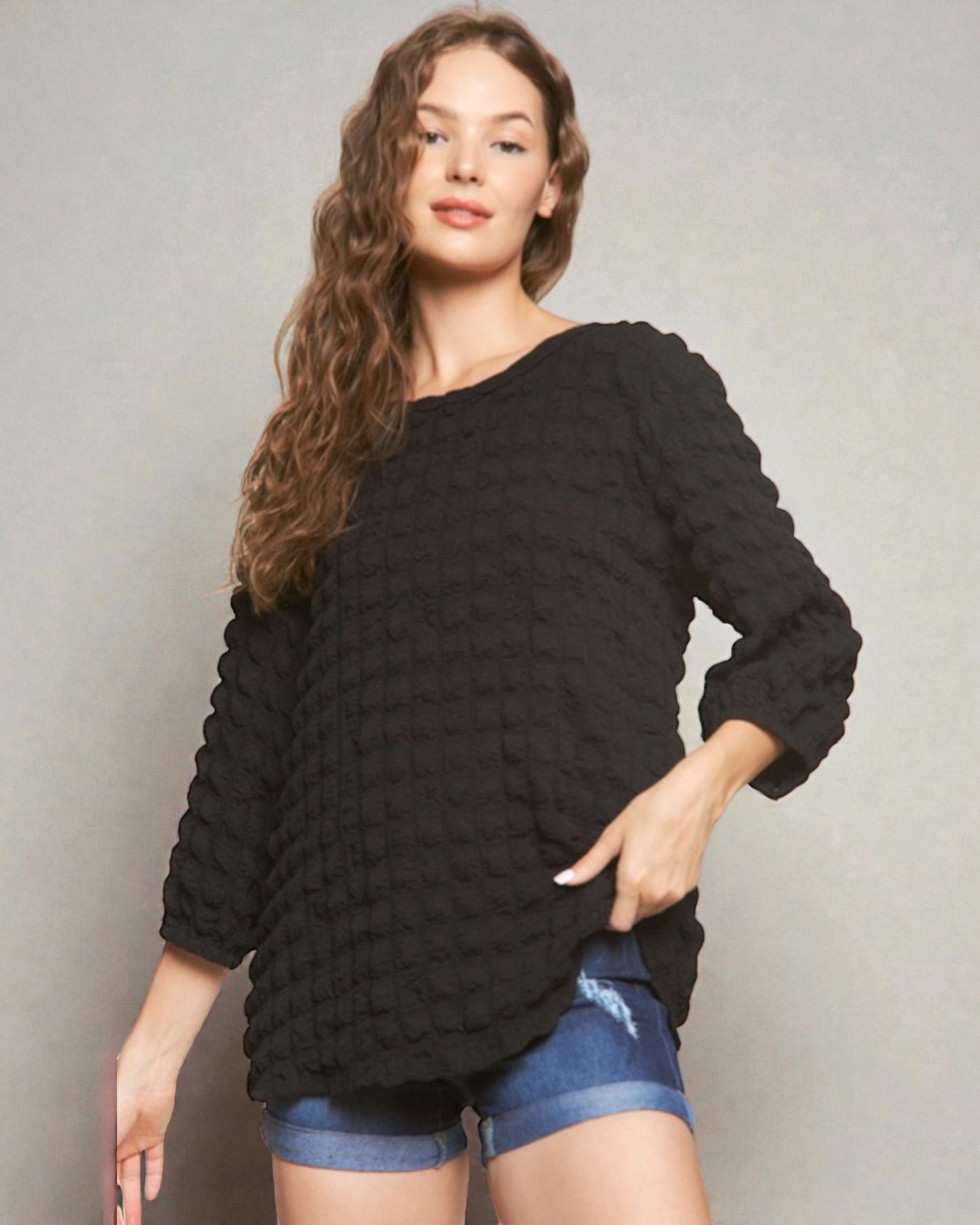 Woman wearing a black textured sweater and denim shorts against a plain background