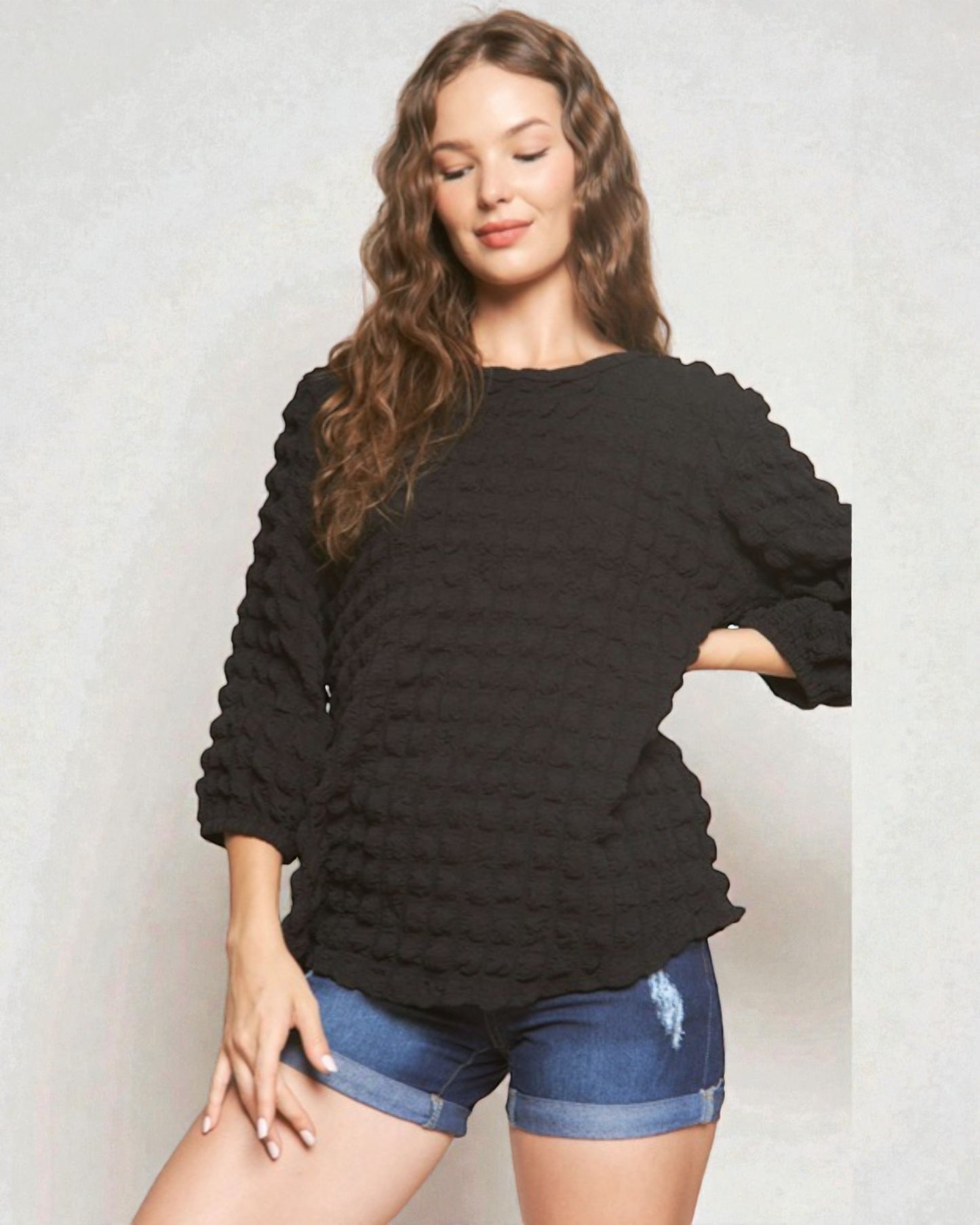 Woman wearing a black textured sweater and denim shorts against a plain background