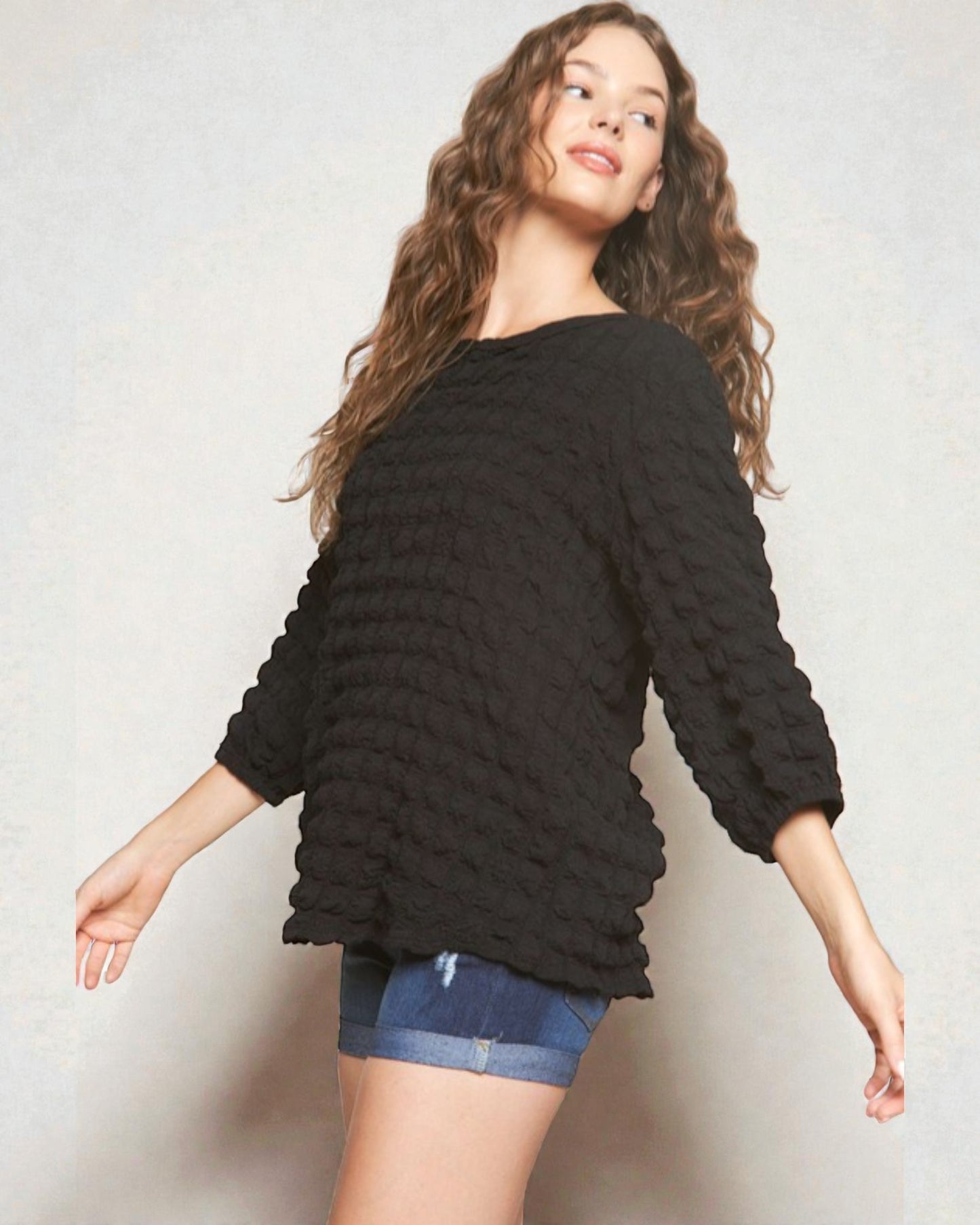 Woman wearing a black textured sweater and denim shorts on a light background