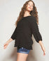 Woman wearing a black textured sweater and denim shorts on a light background
