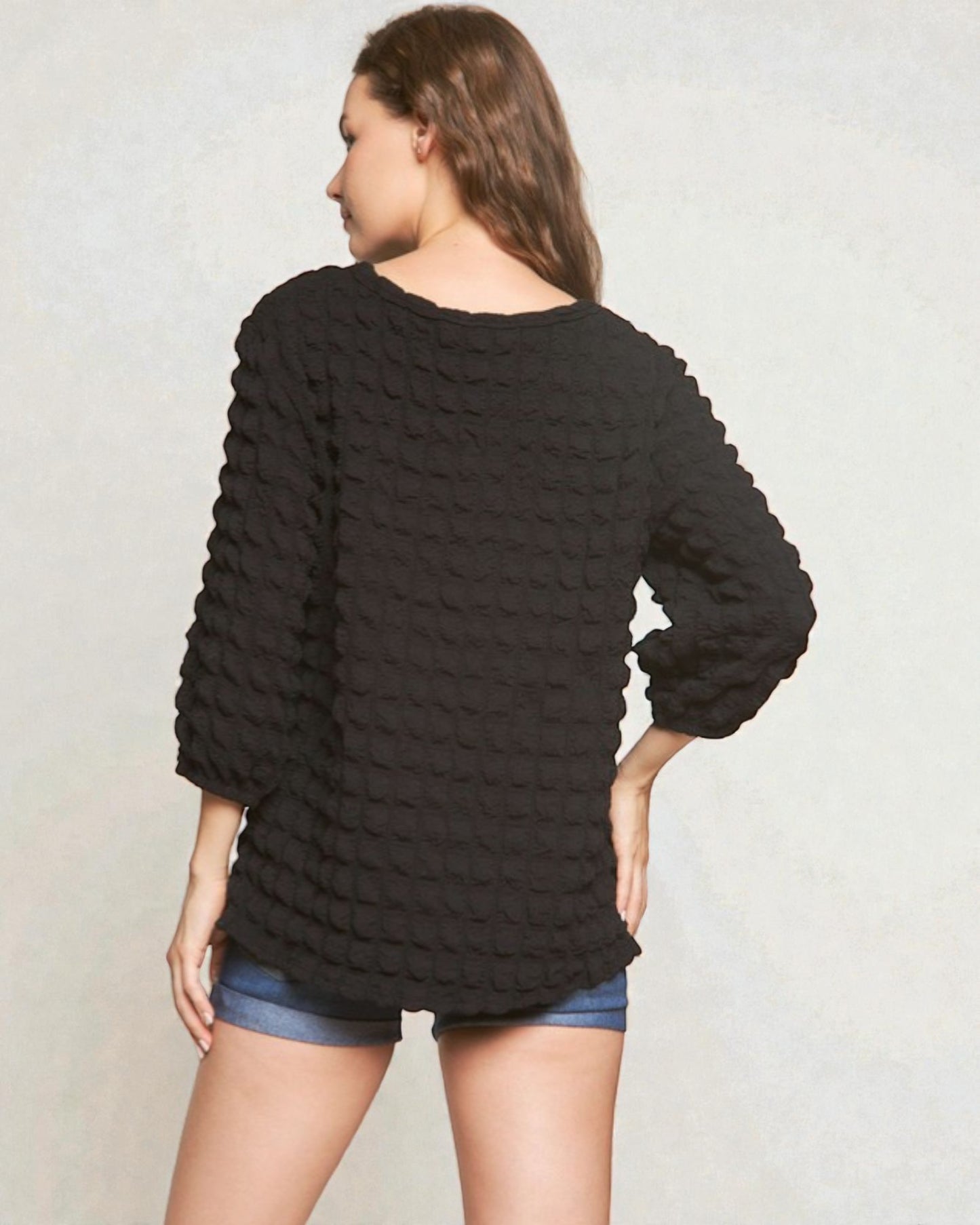 Woman wearing a black textured sweater and denim shorts on a plain background