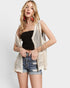 Woman wearing a black top, denim shorts, and a beige crochet cardigan on a white background