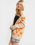 Woman wearing a beige cardigan with orange heart patterns on a white background