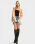 Woman wearing a patterned cardigan, black top, denim shorts, and knee-high boots on a white background