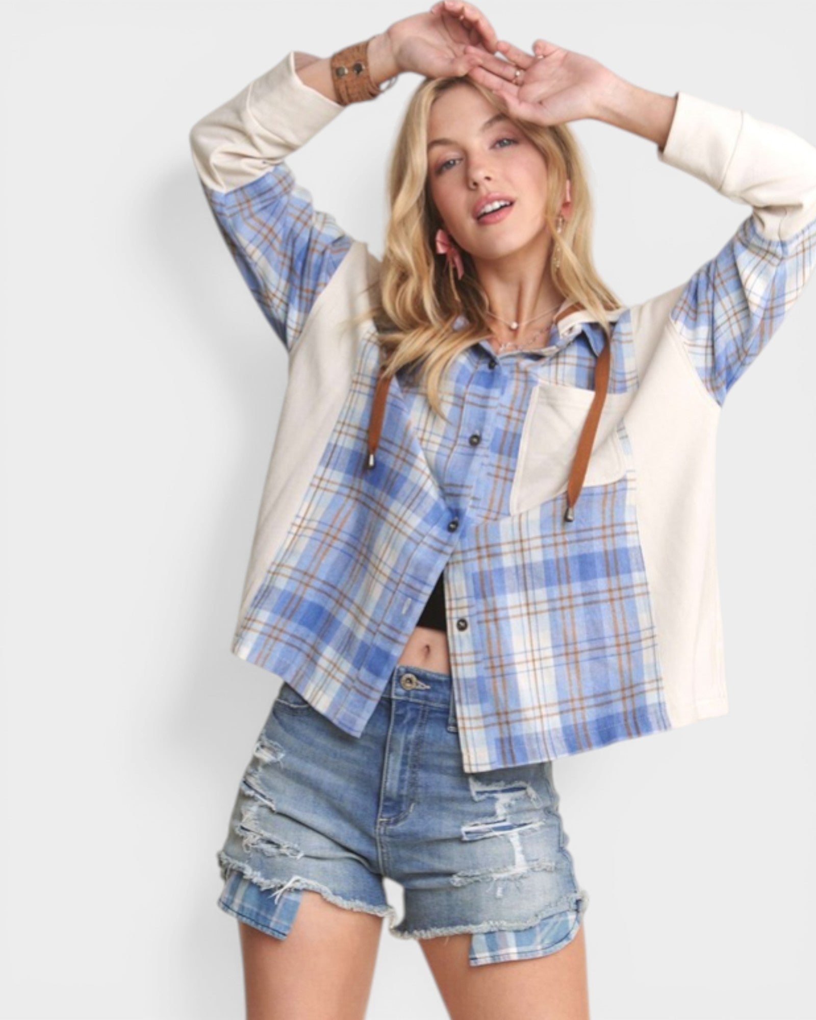 Woman wearing a blue plaid shirt over a white long-sleeve shirt with denim shorts on a white background