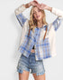 Woman wearing a blue plaid shirt over a white long-sleeve shirt with denim shorts on a white background