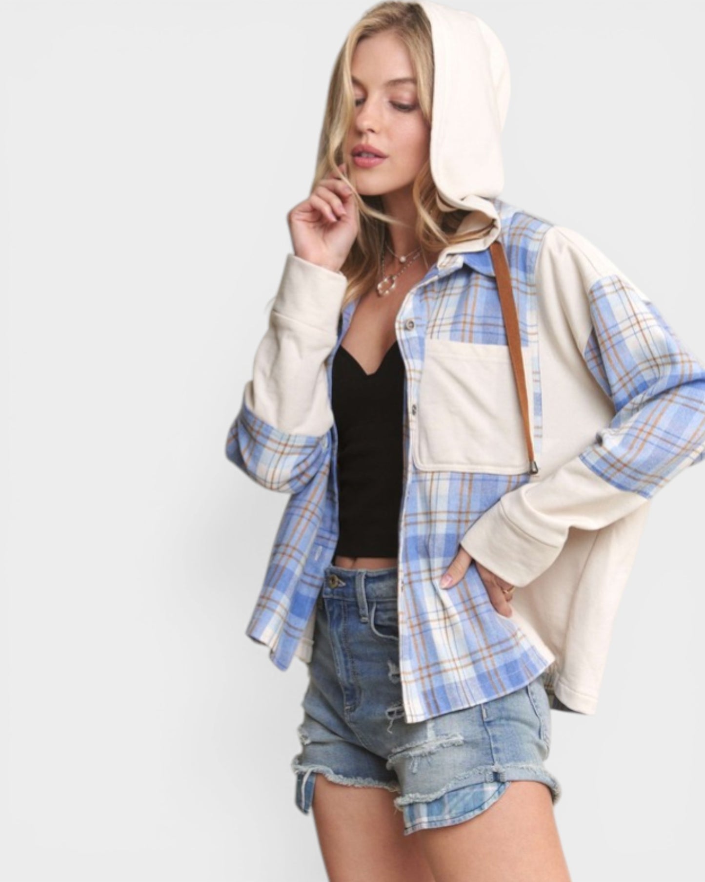 Woman wearing a plaid shirt over a hoodie with denim shorts on a white background