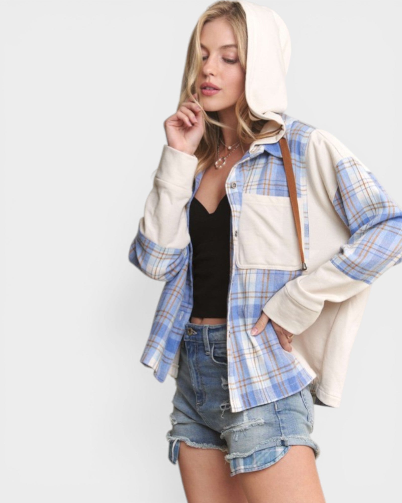 Woman wearing a plaid shirt over a hoodie with denim shorts on a white background