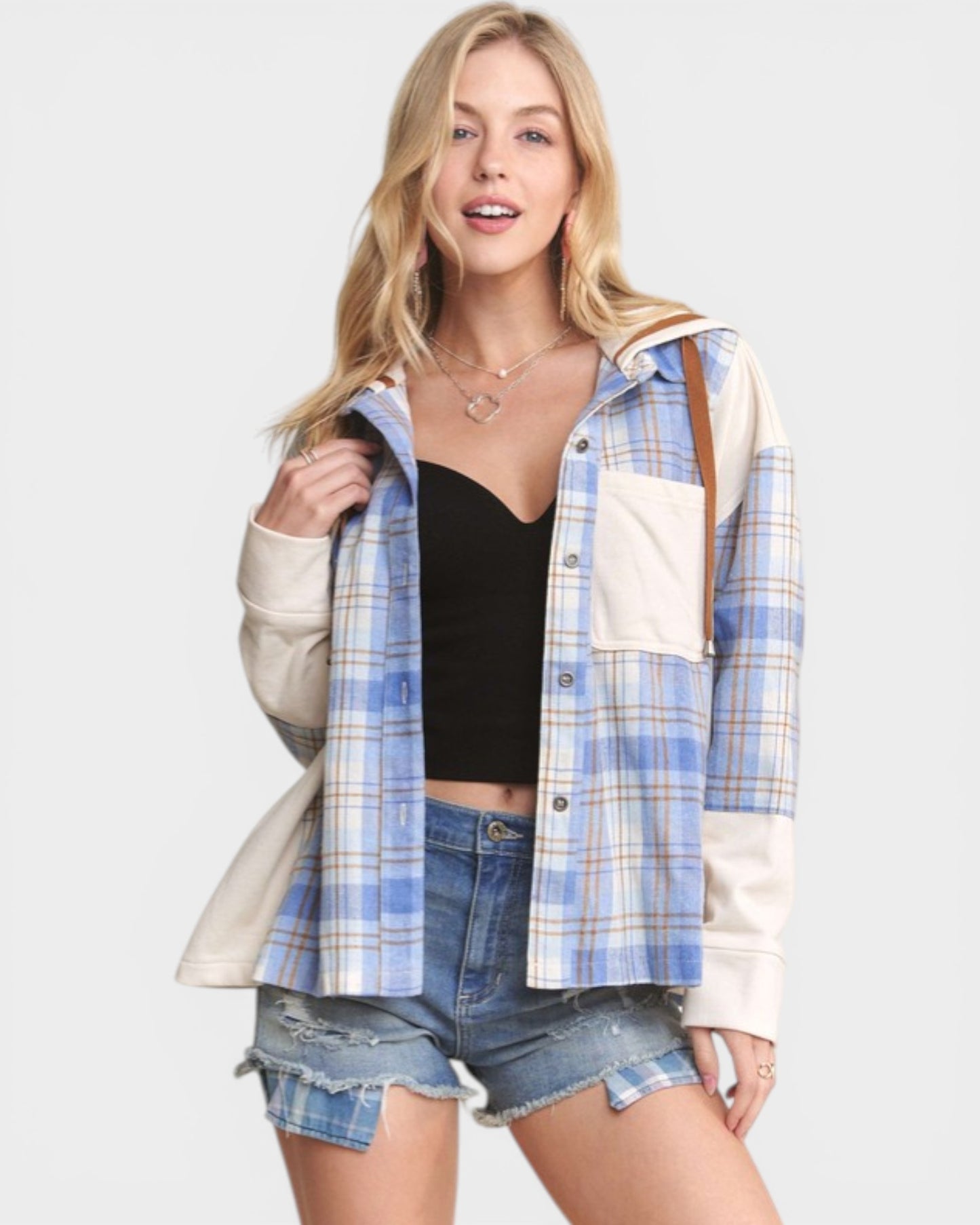 Woman wearing a plaid shirt over a black crop top and denim shorts on a white background