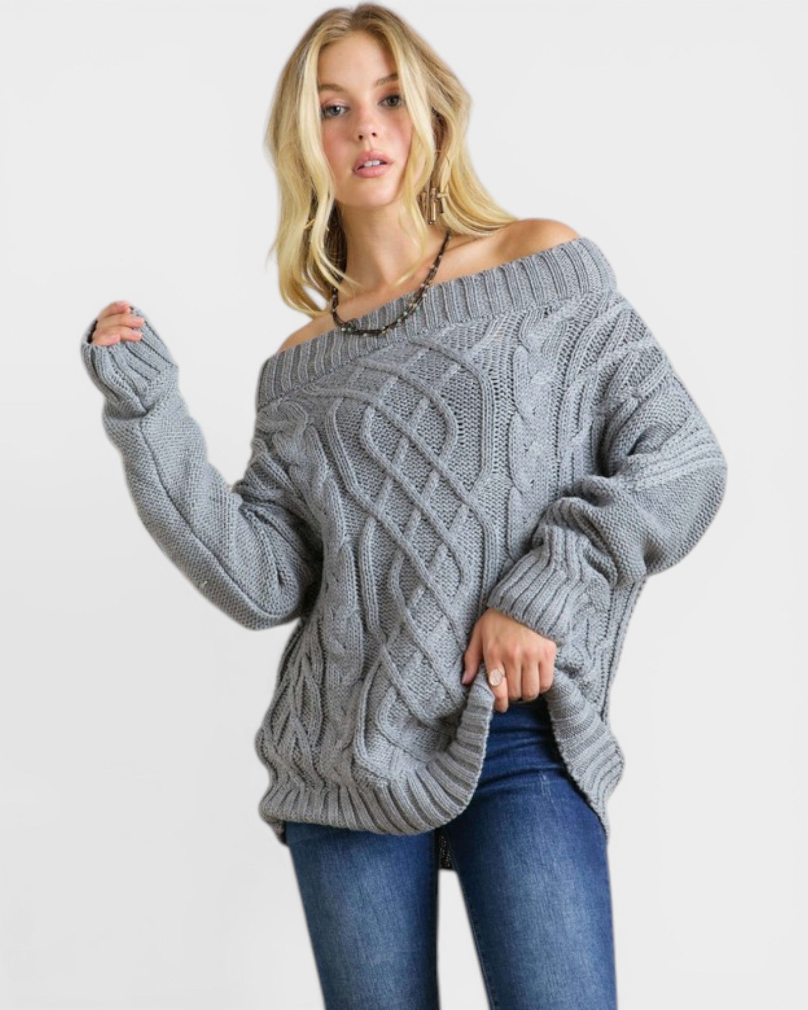 Woman wearing a gray off-shoulder cable knit sweater on a white background