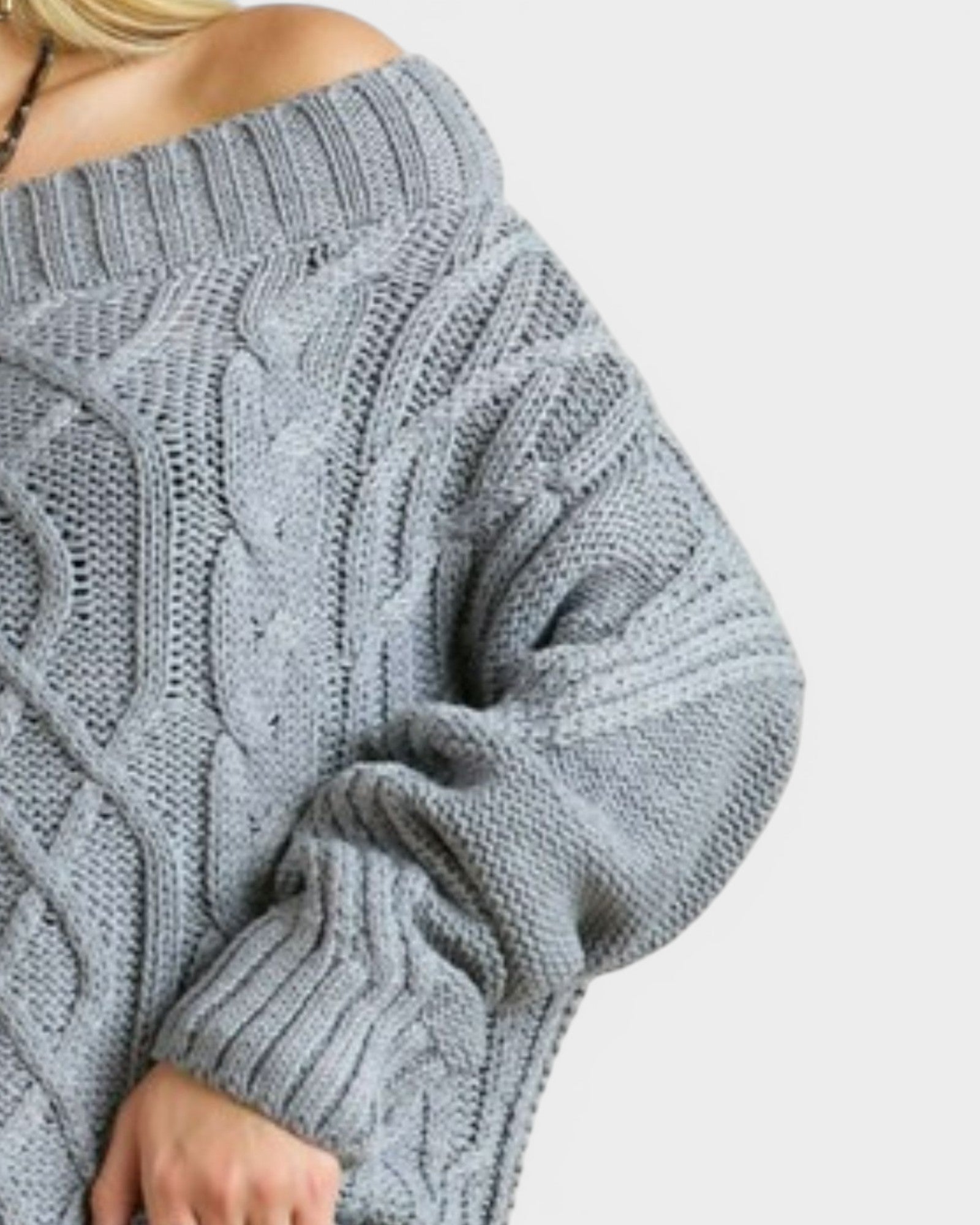 Close-up of a person wearing a gray cable knit sweater on a light gray background