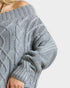 Close-up of a person wearing a gray cable knit sweater on a light gray background