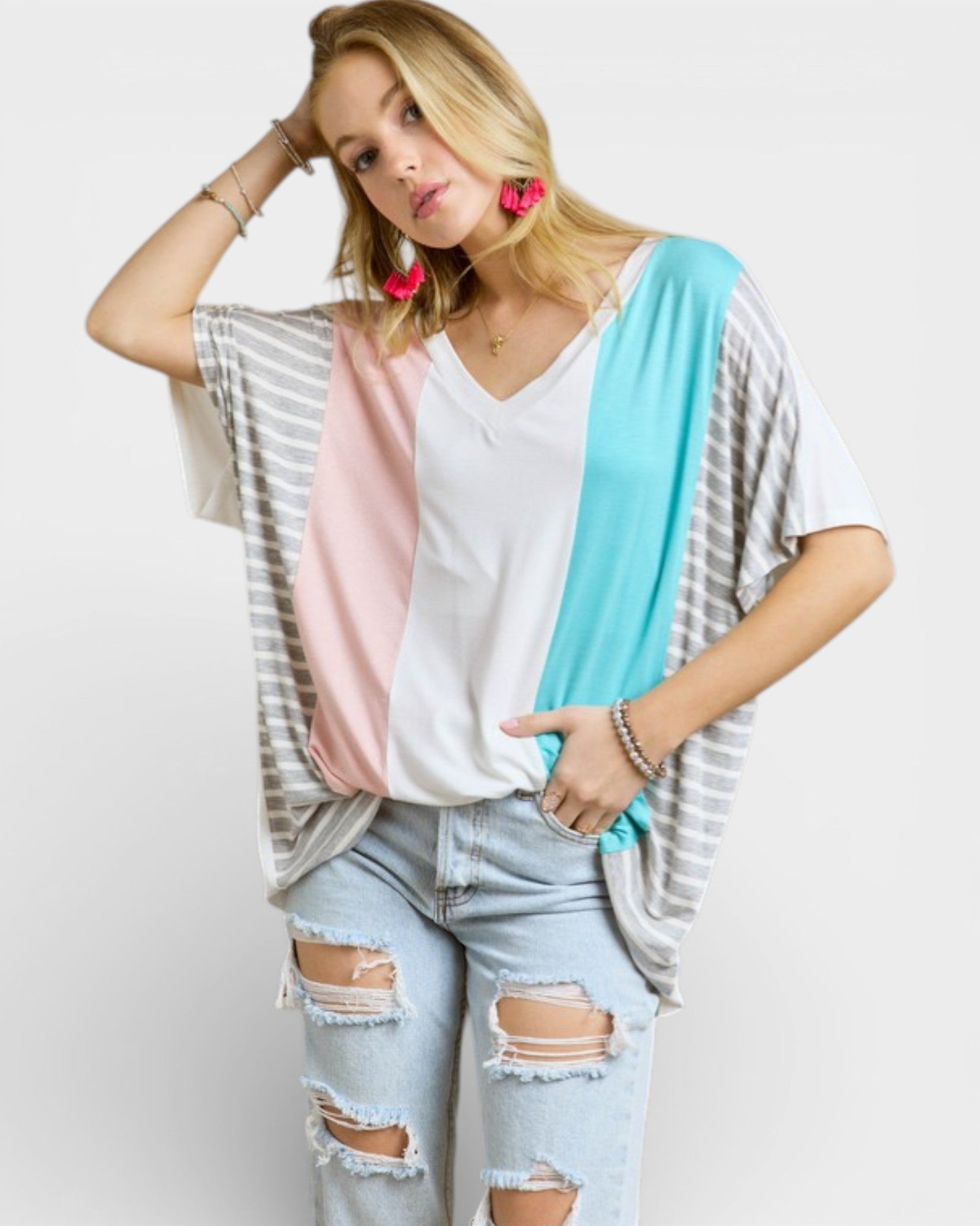 Woman wearing a layered outfit with a white top, pink cardigan, and ripped jeans on a plain background