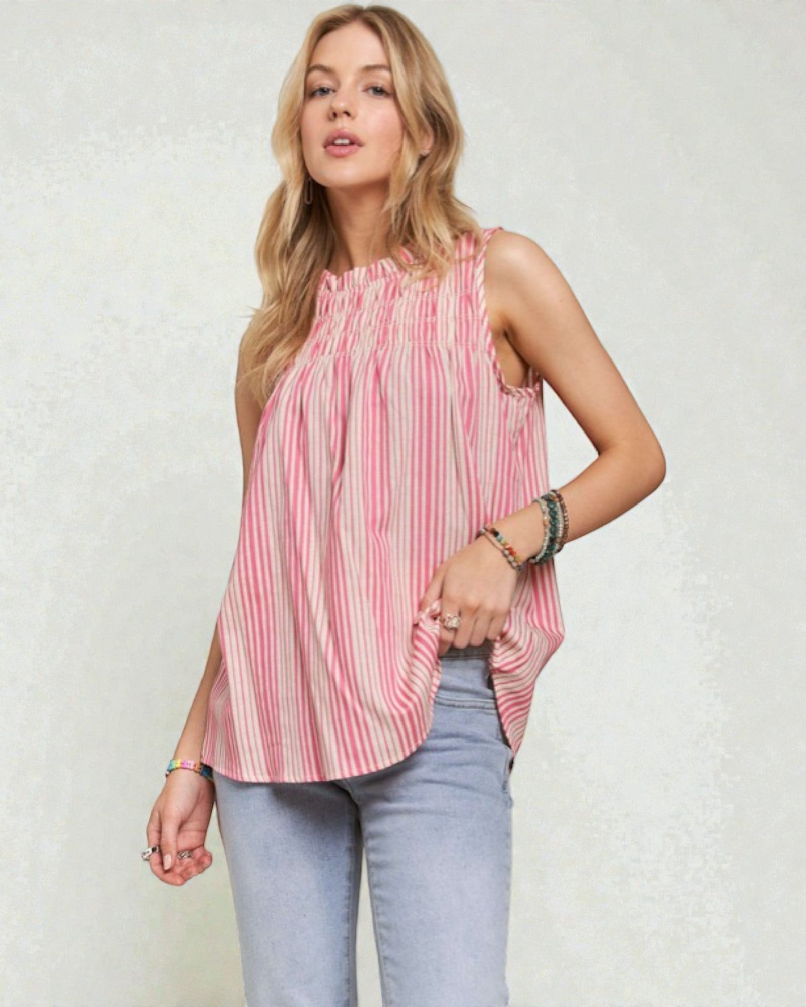 Woman wearing a pink and white striped sleeveless top with light blue jeans on a plain background