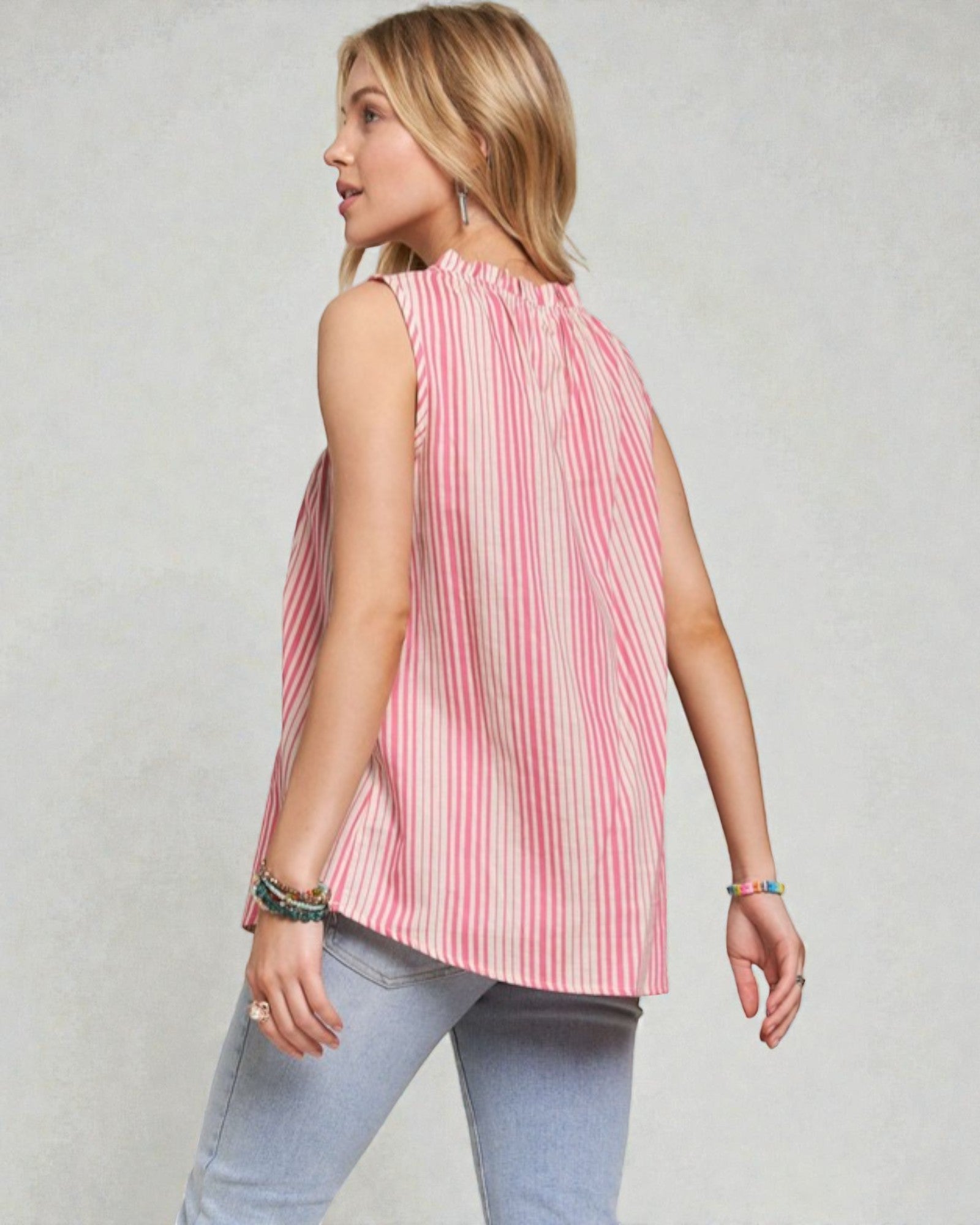 Woman wearing a pink striped sleeveless top and light blue jeans on a plain background