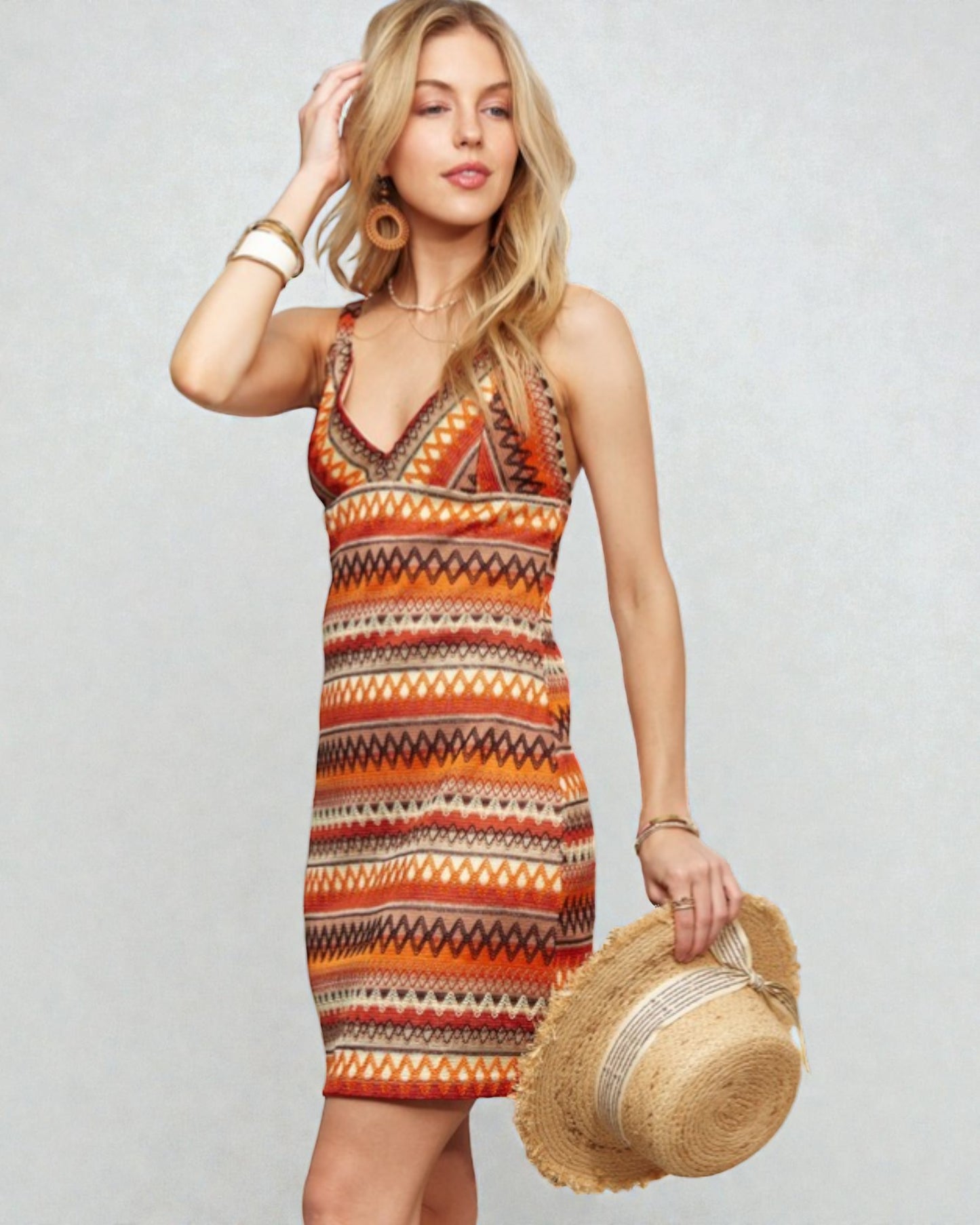 Woman wearing a patterned dress holding a straw hat against a plain background