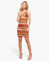 A woman modeling a sleeveless bodycon mini dress with a colorful geometric pattern in orange, brown, black, and white, set against a plain light gray background.