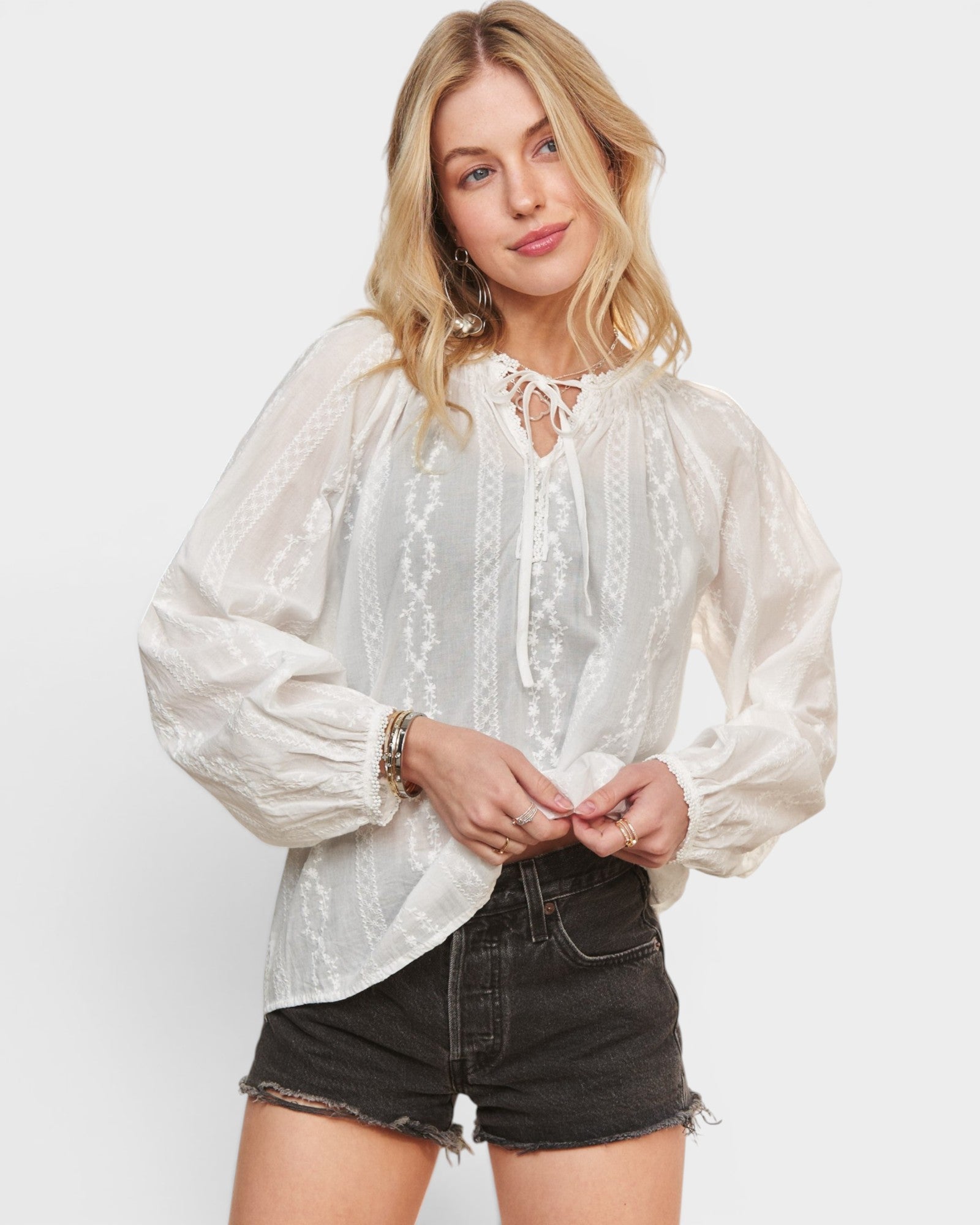 Woman wearing a white embroidered blouse and black shorts on a plain background