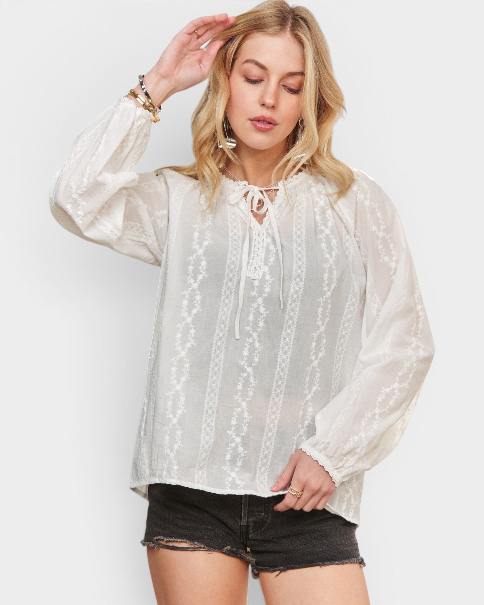 Woman wearing a white lace blouse with long sleeves on a plain background