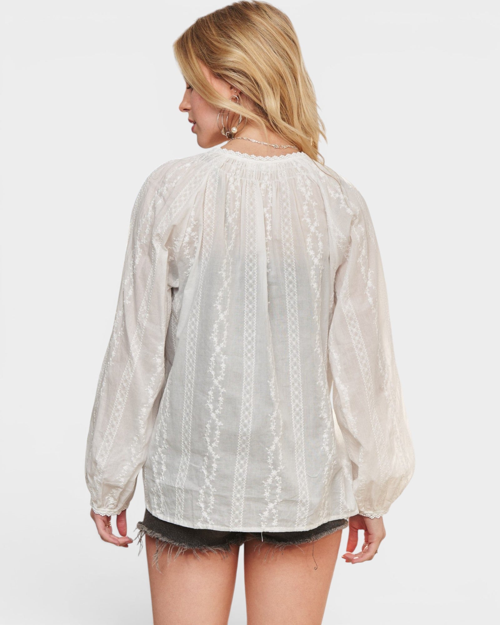 Woman wearing a sheer white blouse with long sleeves on a white background