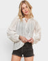 Woman wearing a white embroidered blouse and black shorts on a plain background