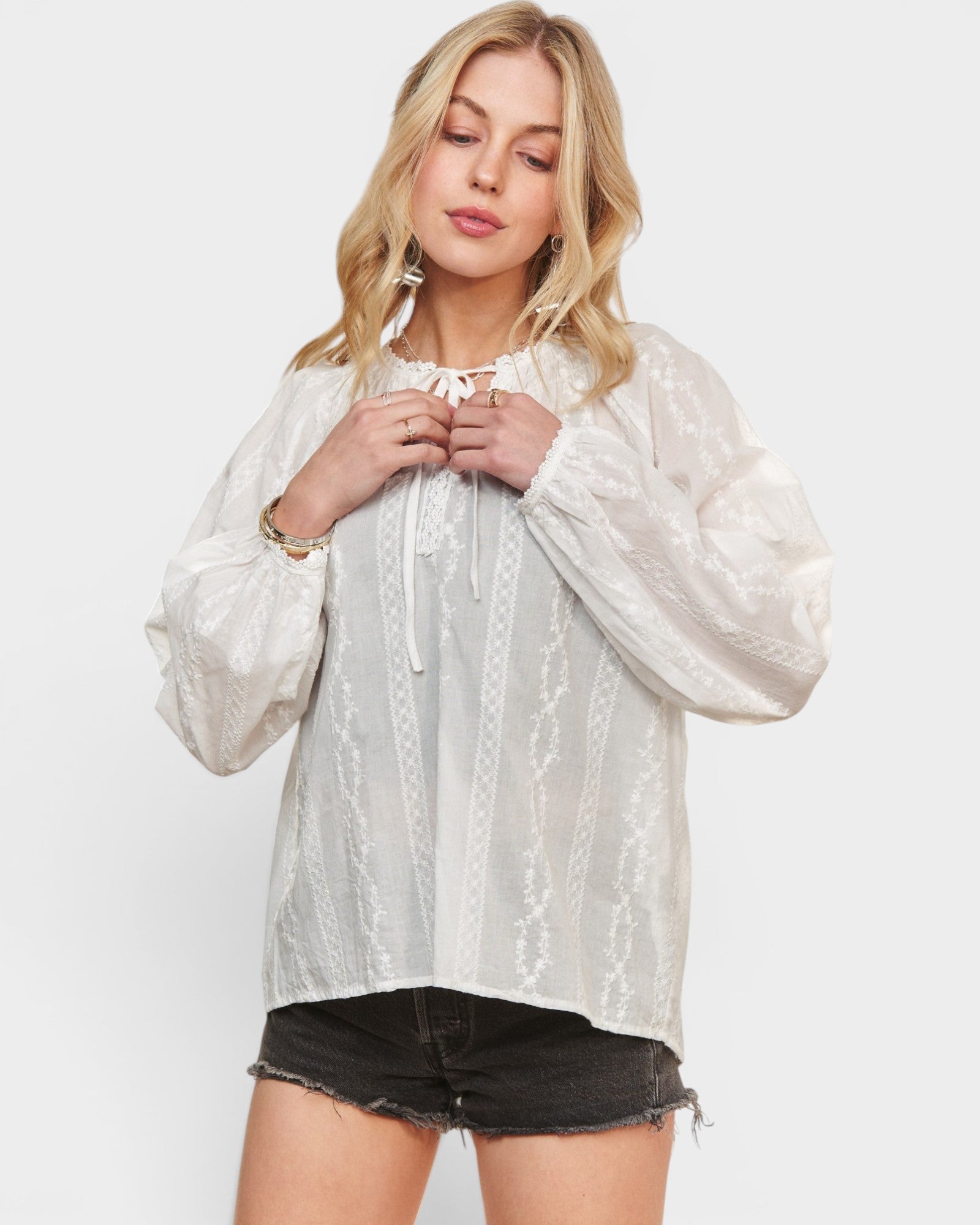 Woman wearing a white lace blouse with black shorts on a white background
