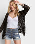 Woman wearing a black lace cardigan, white top, and denim shorts on a light gray background