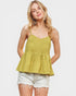 Woman wearing a green smocked top and white shorts on a plain background