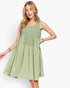 A woman modeling a sleeveless sage green dress with a buttoned bodice and a flared skirt, set against a plain white studio background.