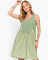 A woman modeling a sleeveless light sage green dress with a buttoned bodice and gathered skirt, posed against a clean white studio background.