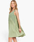 A woman modeling a sleeveless sage green dress with a gathered, tiered skirt against a plain white studio background.