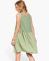 A woman modeling a sleeveless light sage green dress from the back, showing a gathered waist seam and scalloped edge, against a plain white background.