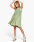 A woman modeling a sleeveless sage green dress with a gathered waist and front button placket, paired with beige lace-up ankle boots, against a plain white studio background.