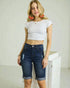 Woman wearing a white crop top and blue denim shorts against a plain background