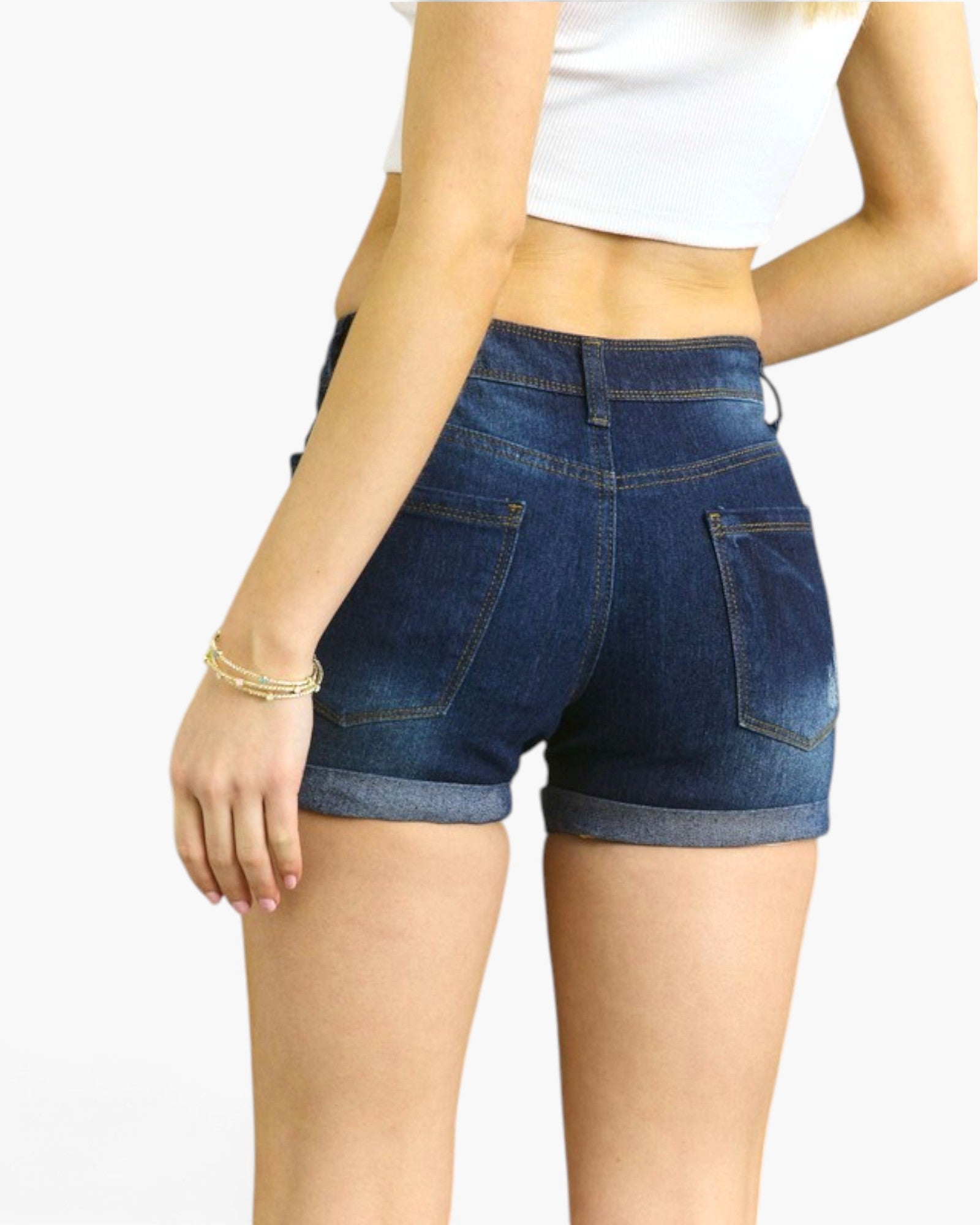 A person shown from the back wearing dark blue denim shorts with rolled hems and a white cropped top, against a plain light background.